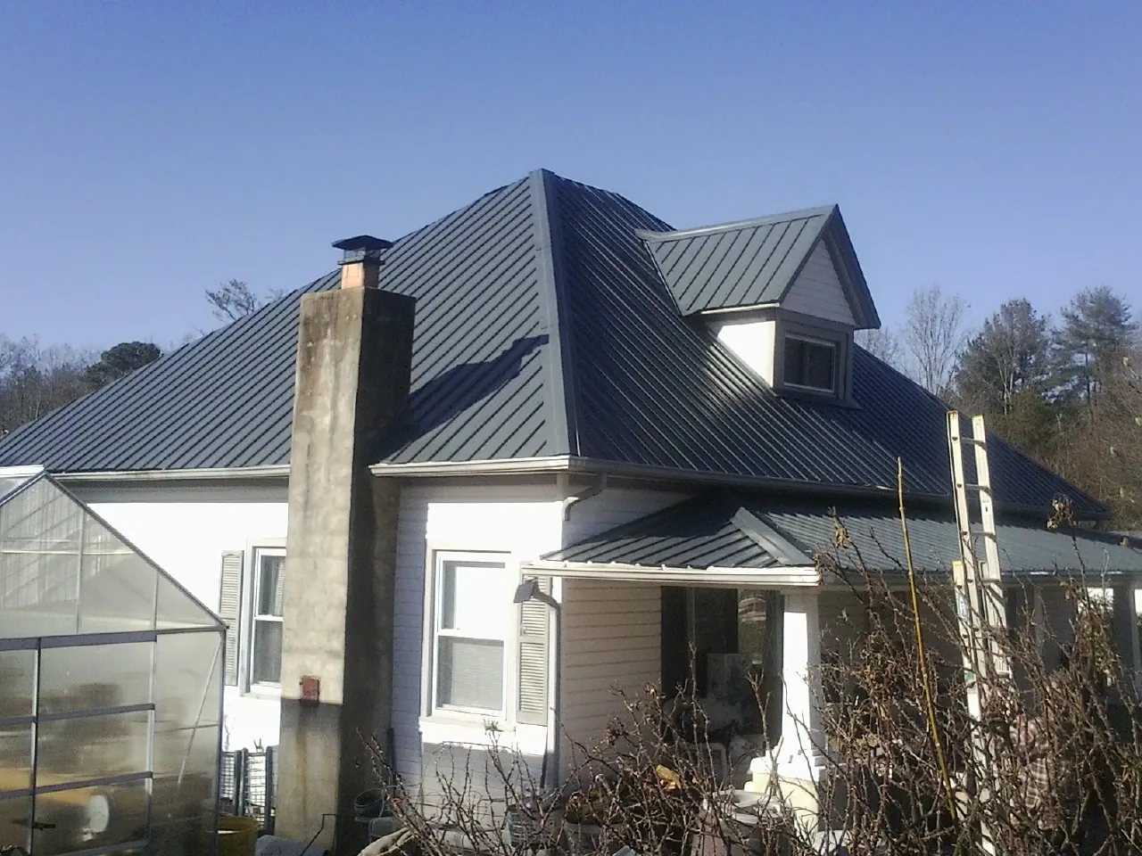 Dark blue standing seam metal roof on a white farmhouse with dormer — Slate & Tile Roof Repair by Roofing Brothers in Gleason