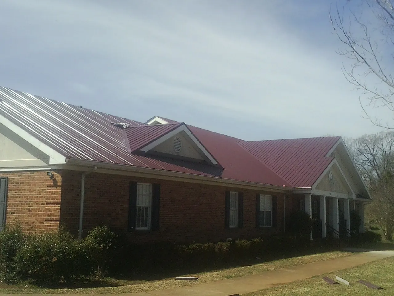 Red metal roof with gabled entries on a long brick building, from a Hail Damage Roof Repair job in Gleason