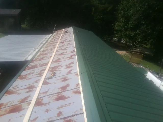 Old rusted panels beside newly installed green metal roofing — Wind Damage Roof Repair by Roofing Brothers in Gleason