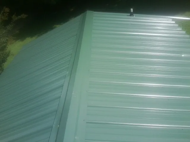 New green metal panels meeting at the ridge of a roof — Flat Roof Repair work by our crew in Gleason