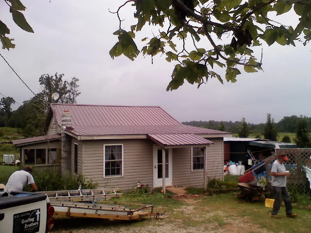 Crew finishing a mauve metal roof on a small farmhouse in Gleason
