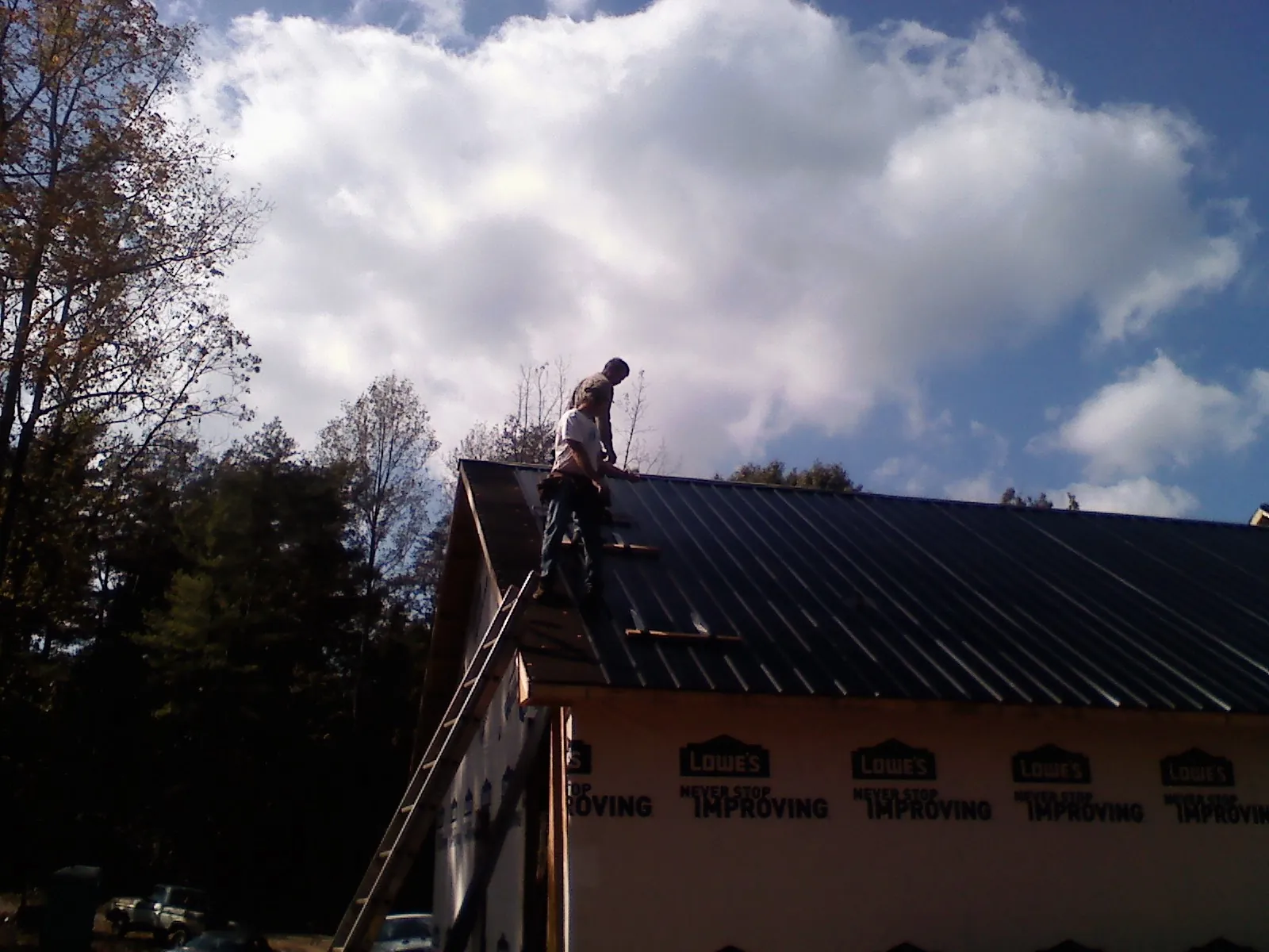 Roofer fastening dark metal panels high against a cloudy sky, from a Roof Inspection job in Gleason