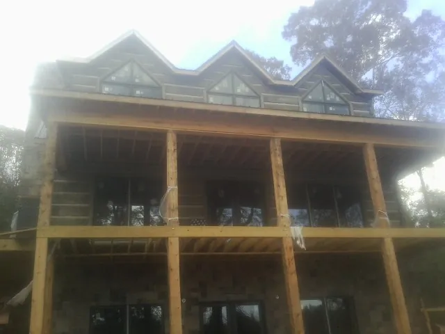 Dormers and porch framing on a large log home under construction — Roof Coating work by our crew in Gleason