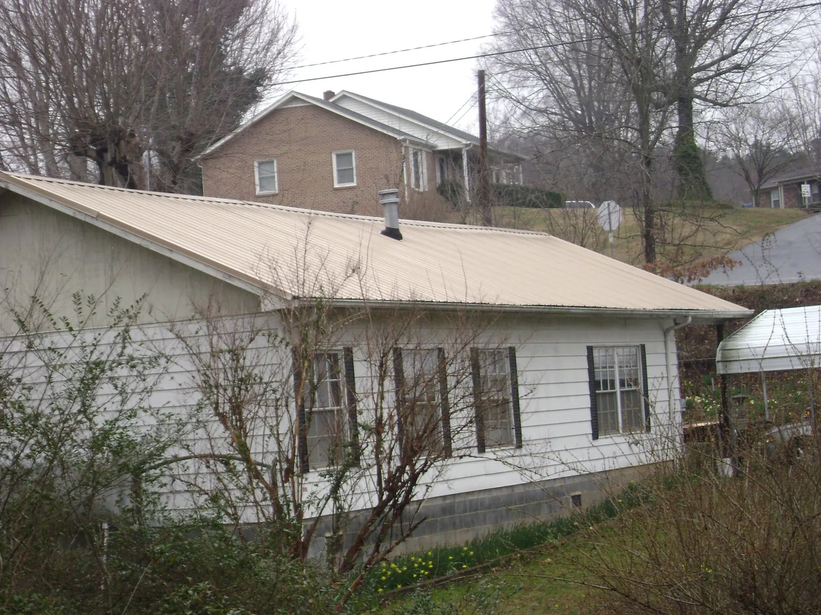 Tan metal roof on a white sided house set into a hillside — Commercial Roofing by Roofing Brothers in Gleason