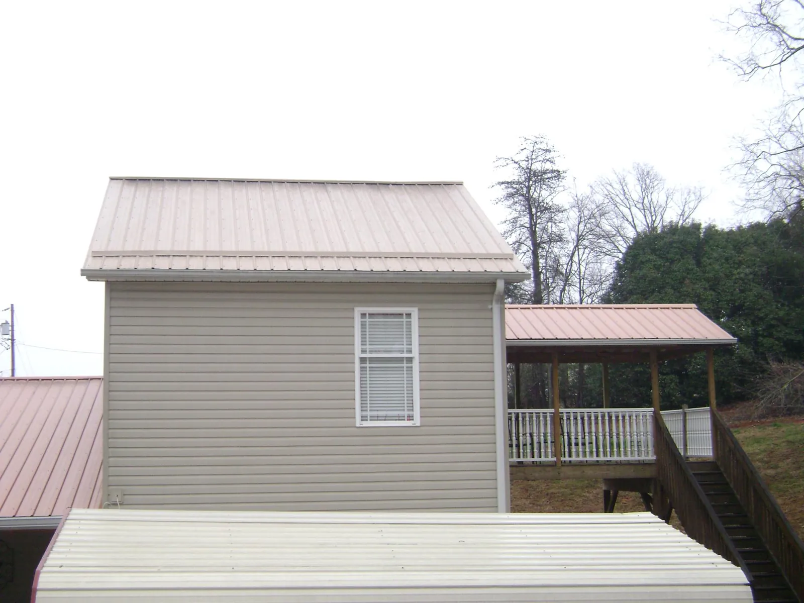 Tan metal roofs on a two story addition and attached porch, from a Roof Replacement job in Gleason